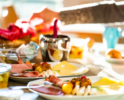 Ein reichhaltig gedeckter Frühstückstisch mit: Wurst, Käse, Obst, Marmelade, Nutella, Brötchen, Croissants, Obstsalat, Kaffee und weiteren Getränken.