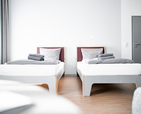 Zwei einzelne moderne Betten in einem Zweibettzimmer. Auf den Betten liegen zwei Handtücher.