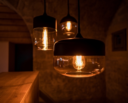 Lampen Caponniere Drei Lampen hängen in der Caponniere. Die Lampenschirme sind aus Glas und sind rund geformt. Das Licht erstrahlt in einem warmen Gelbton. Das Zimmer ist dunkel.