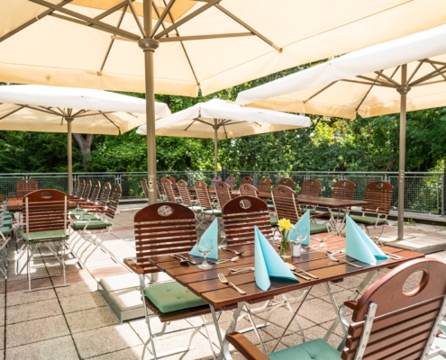 Terrasse des Gästehauses Dreibrunnen Drei schattige Plätze auf der sonnendurchfluteten Terrasse des Gästehauses Dreibrunnen. Der Tisch ist mitBesteck und türkisen Servietten gedeckt.